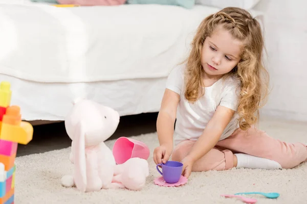 Adorabile bambino che gioca con il giocattolo del coniglio e bicchieri di plastica nella stanza dei bambini — Foto stock