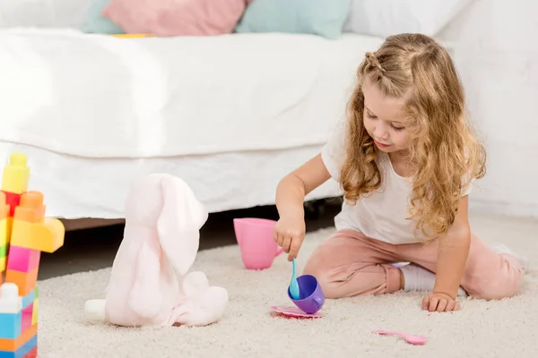 Adorabile bambino in età prescolare che gioca con il giocattolo del coniglio e bicchieri di plastica nella stanza dei bambini — Foto stock