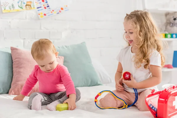 Tout-petit et les sœurs de maternelle jouant avec la trousse de premiers soins dans la chambre des enfants — Photo de stock