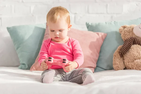 Adorable kid in pink shirt holding pink joystick on bed in children room — Stock Photo