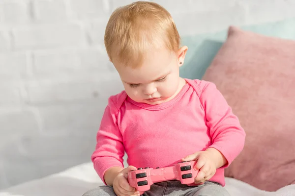 Adorable enfant en chemise rose tenant joystick rose sur le lit dans la chambre des enfants — Photo de stock