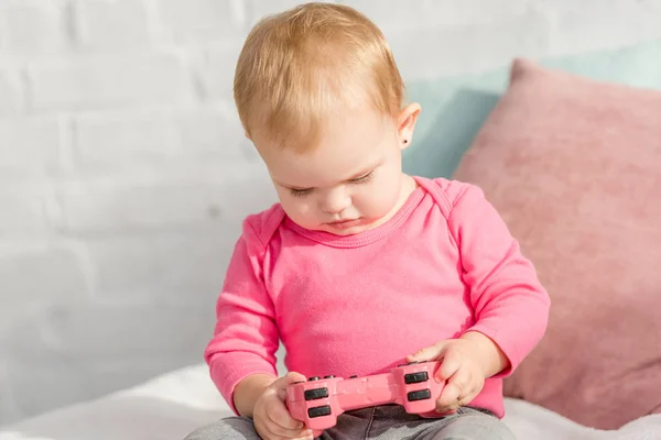 Adorabile bambino in camicia rosa con joystick rosa sul letto nella stanza dei bambini — Foto stock