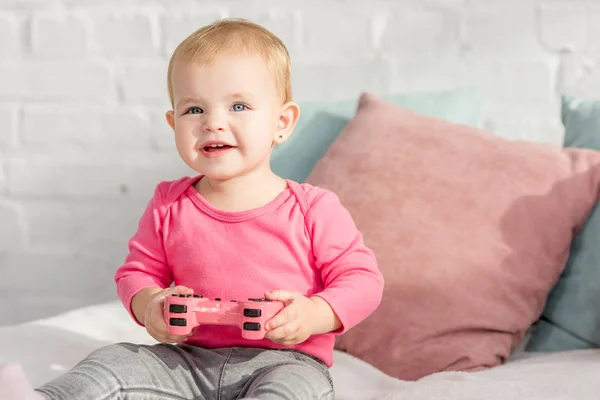 Smiling adorable kid in pink shirt holding pink joystick on bed in children room — Stock Photo