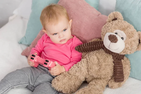 Angry adorable kid in pink shirt holding pink joystick on bed in children room — Stock Photo