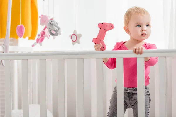 Adorable kid in pink shirt holding pink joystick and standing in crib — Stock Photo