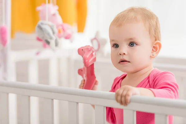 Adorable child in pink shirt holding pink joystick in crib — Stock Photo