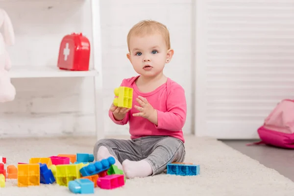 Чарівна дитина грає з конструктором на килимі в дитячій кімнаті — стокове фото