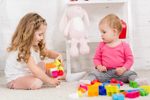 Adorable sisters playing with constructor together on carpet in children room — Stock Photo