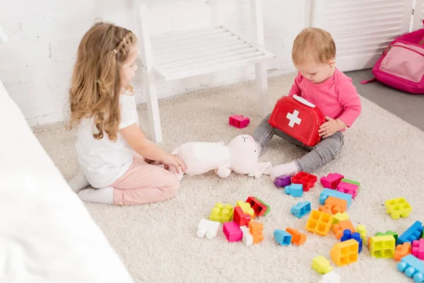 Adorables hermanas jugando con juguetes en la alfombra en la habitación de los niños - foto de stock