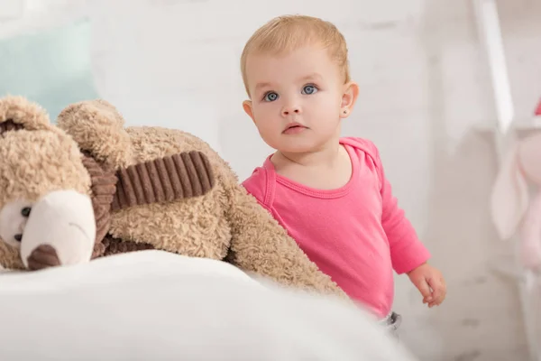 Entzückendes Kind, das neben Teddybär steht und im Kinderzimmer nach oben schaut — Stockfoto