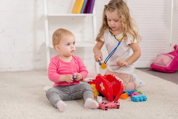 Adorável pré-escolar e irmãs criança brincando com kit de primeiros socorros na sala de crianças — Fotografia de Stock