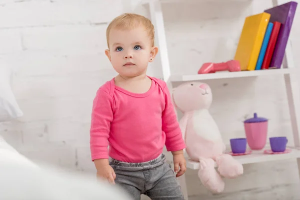 Adorable enfant en chemise rose debout et levant les yeux dans la chambre des enfants — Photo de stock