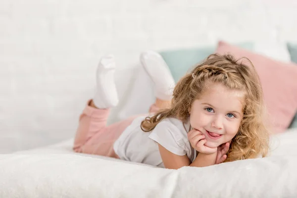 Lächelnd entzückendes glückliches Kind, das im Kinderzimmer auf dem Bett liegt und in die Kamera schaut — Stockfoto