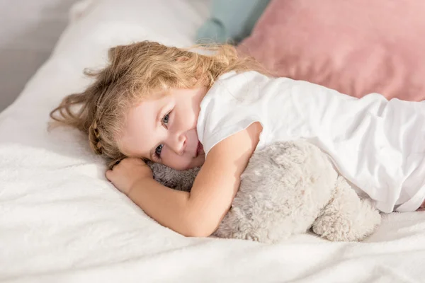 Sonriendo adorable feliz niño acostado en la cama en la habitación de los niños y mirando hacia otro lado - foto de stock