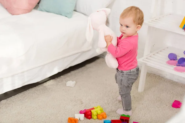 Adorabile bambino in camicia rosa che tiene il giocattolo del coniglio nella stanza dei bambini — Foto stock