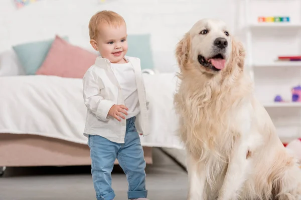 Smiling adorable kid looking at golden retriever dog in children room — Stock Photo