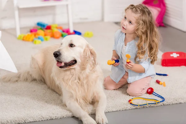 Adorable kid pretending veterinarian and fluffy examining golden retriever in children room — Stock Photo