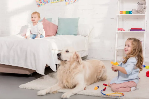 Foco seletivo de criança adorável brincando com golden retriever na sala de crianças — Fotografia de Stock