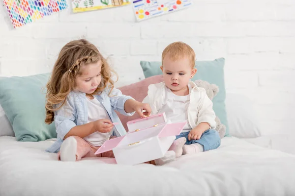 Adorable preschooler and toddler sisters playing on bed in children room — Stock Photo