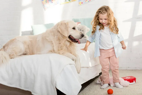 Adorable kid standing near bed with dog in children room — Stock Photo