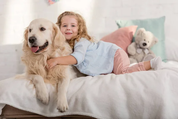Adorable happy kid and golden retriever lying on bed in children room — Stock Photo