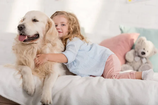 Adorable enfant étreignant golden retriever sur le lit dans la chambre des enfants — Photo de stock