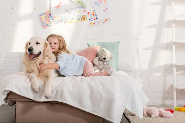 Adorable child hugging cute golden retriever on bed in children room — Stock Photo