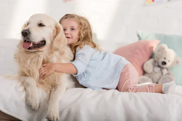 Adorable kid hugging golden retriever dog on bed in children room — Stock Photo