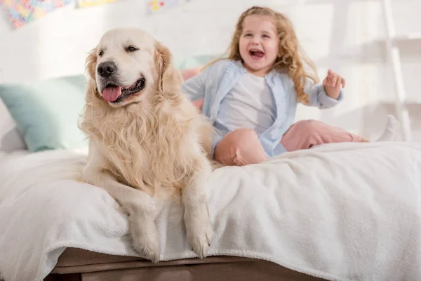 Laughing adorable kid and cute golden retriever sitting on bed together in children room — Stock Photo