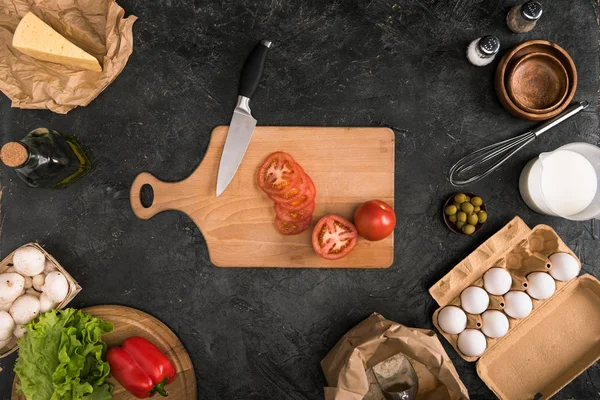 Вид сверху на нарезанные помидоры на доске и ингредиенты для пиццы на сером фоне — стоковое фото