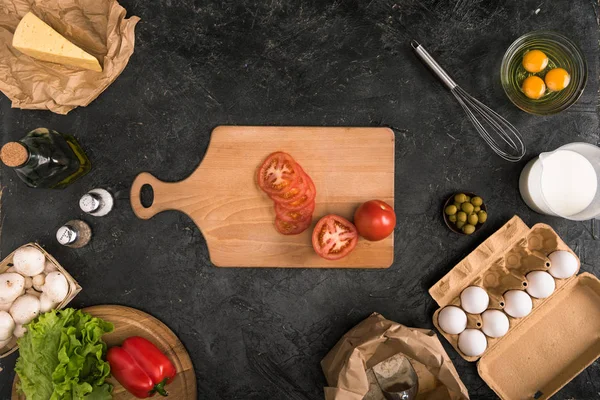 Vista superior de tomates picados sobre tabla de cortar e ingredientes de pizza sobre fondo gris - foto de stock