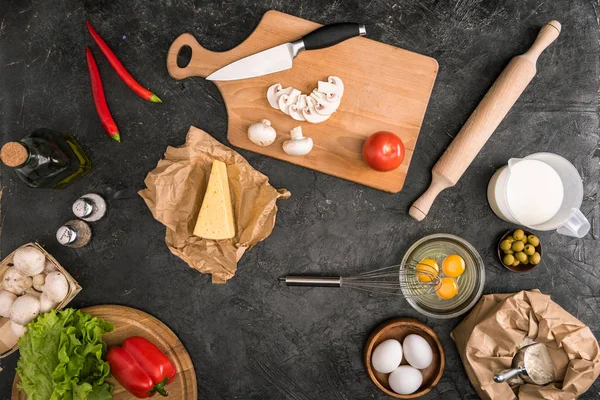 Vista superior de los ingredientes de la pizza y utensilios de cocina sobre fondo gris - foto de stock