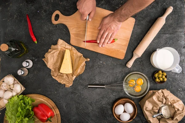 Vista cortada do homem corte pimenta pimenta na placa de corte com ingredientes de pizza em fundo cinza — Fotografia de Stock