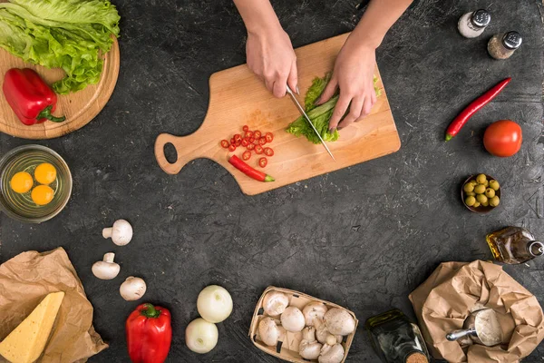 Vista recortada de la mujer picando verduras en la tabla de cortar con ingredientes de pizza sobre fondo gris - foto de stock