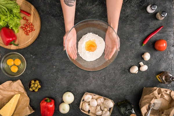 Teilansicht einer Frau mit Schüssel mit Mehl und Pizza-Zutaten auf grauem Hintergrund — Stockfoto