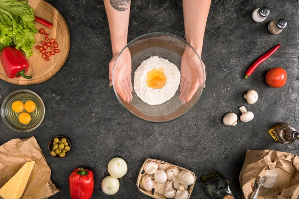 Partial view of woman holding bowl with flour and pizza ingredients on grey background — Stock Photo