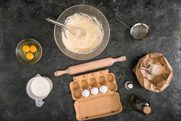 Top view of dough, ingredients and cooking utensils on grey background — Stock Photo