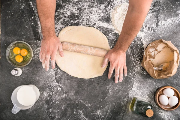 Cropped view of man rolling pizza dough with wooden pin on grey background — Stock Photo