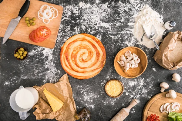 Top view of uncooked pizza and ingredients on grey background with flour — Stock Photo