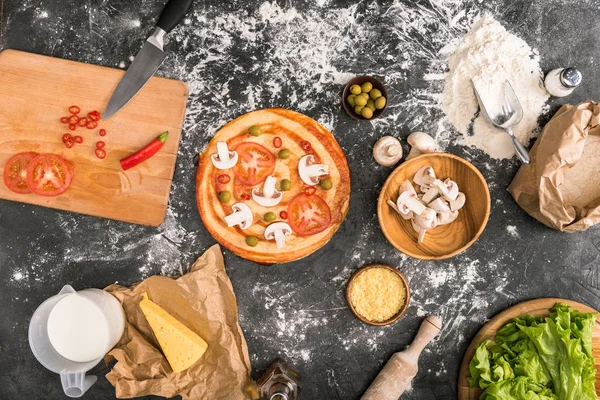 Top view of uncooked pizza and ingredients on grey background with flour — Stock Photo