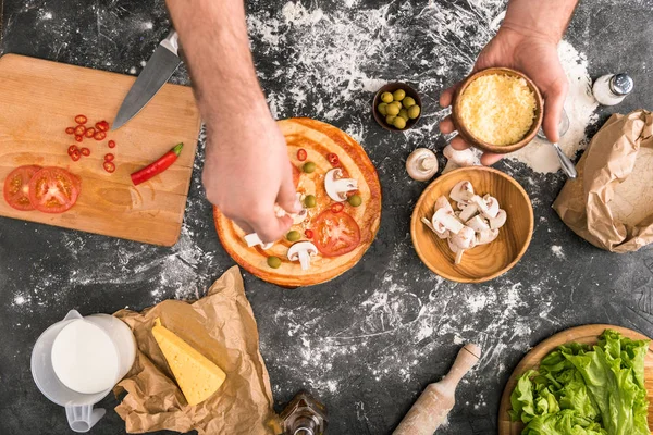 Teilansicht eines Mannes, der Zutaten auf eine Pizza auf grauem Hintergrund mit Mehl legt — Stockfoto