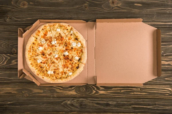 Top view of cheese pizza in cardboard box on wooden table with copy space — Stock Photo