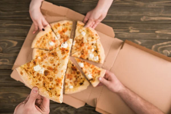 Partial view of friends eating delicious pizza on wooden table — Stock Photo