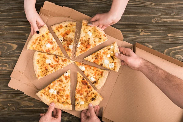 Vista parziale di amici che mangiano pizza al formaggio sul tavolo di legno — Foto stock