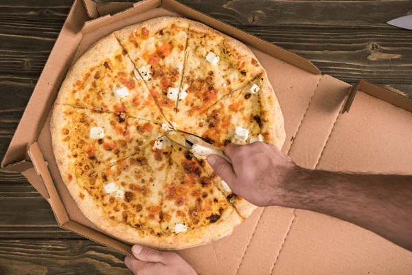 Teilansicht eines Mannes, der mit Messer Käsepizza auf Holztisch schneidet — Stockfoto