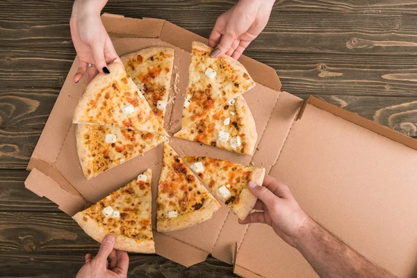 Vista recortada de amigos comiendo pizza de queso en mesa de madera - foto de stock