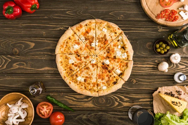 Pizza de queso con ingredientes y verduras en la mesa de madera - foto de stock