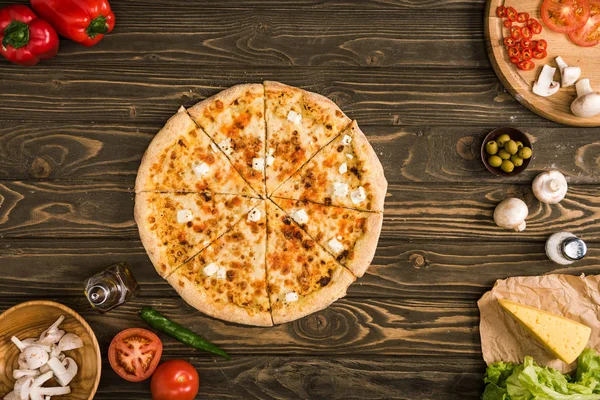 Blick von oben auf Käsepizza mit Zutaten und Gemüse auf Holztisch — Stockfoto