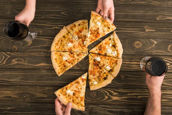 Cropped view of couple having dinner with cheese pizza and red wine at wooden table — Stock Photo