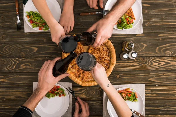 Vue recadrée d'amis griller pendant le dîner avec pizza et salades à la table en bois — Photo de stock